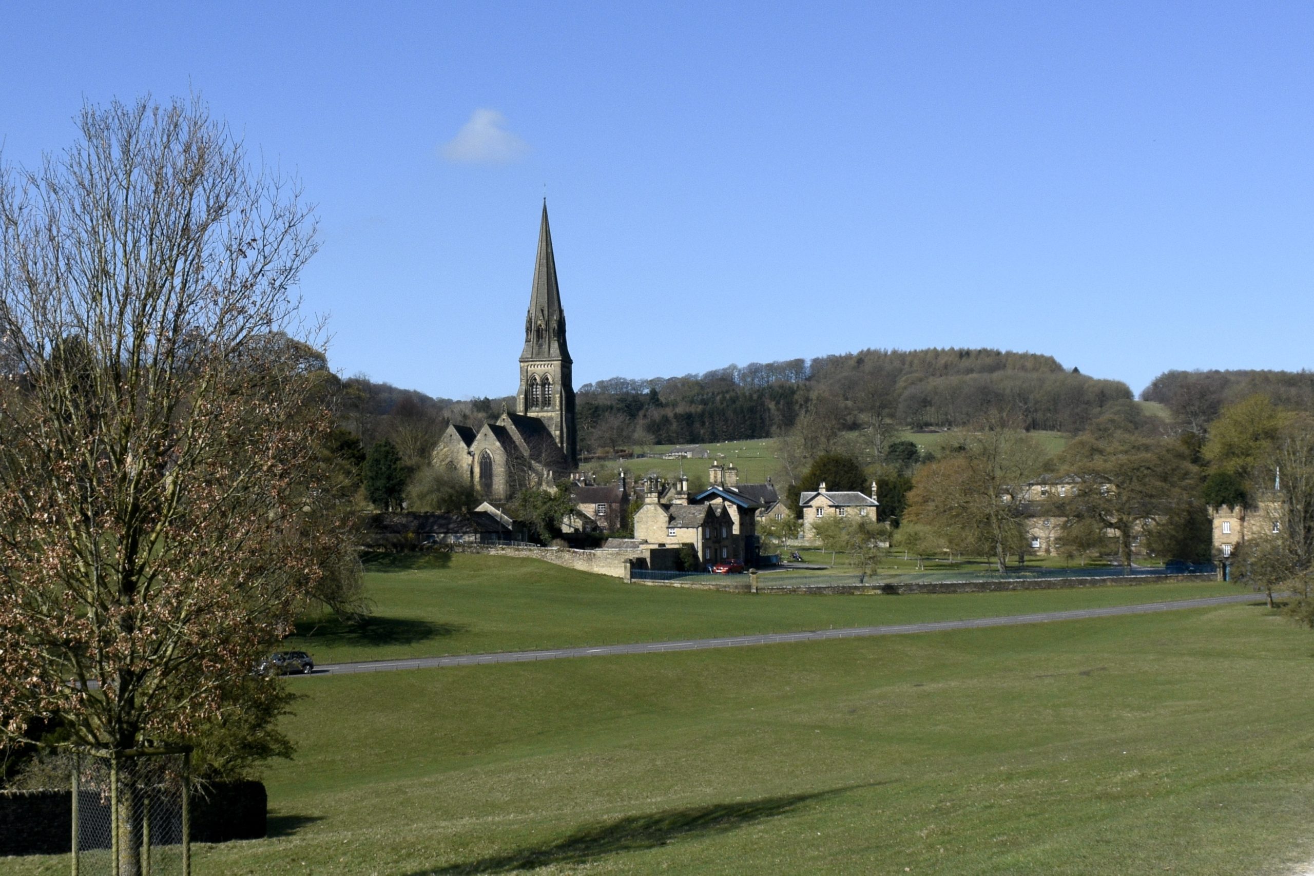 A green parkland with a church spire and stone village buildings under a clear blue sky