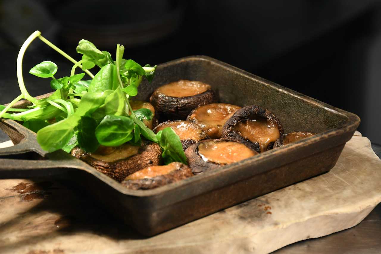 Grilled mushrooms with fresh green herbs served in a dark metal dish, warm brown and green tones