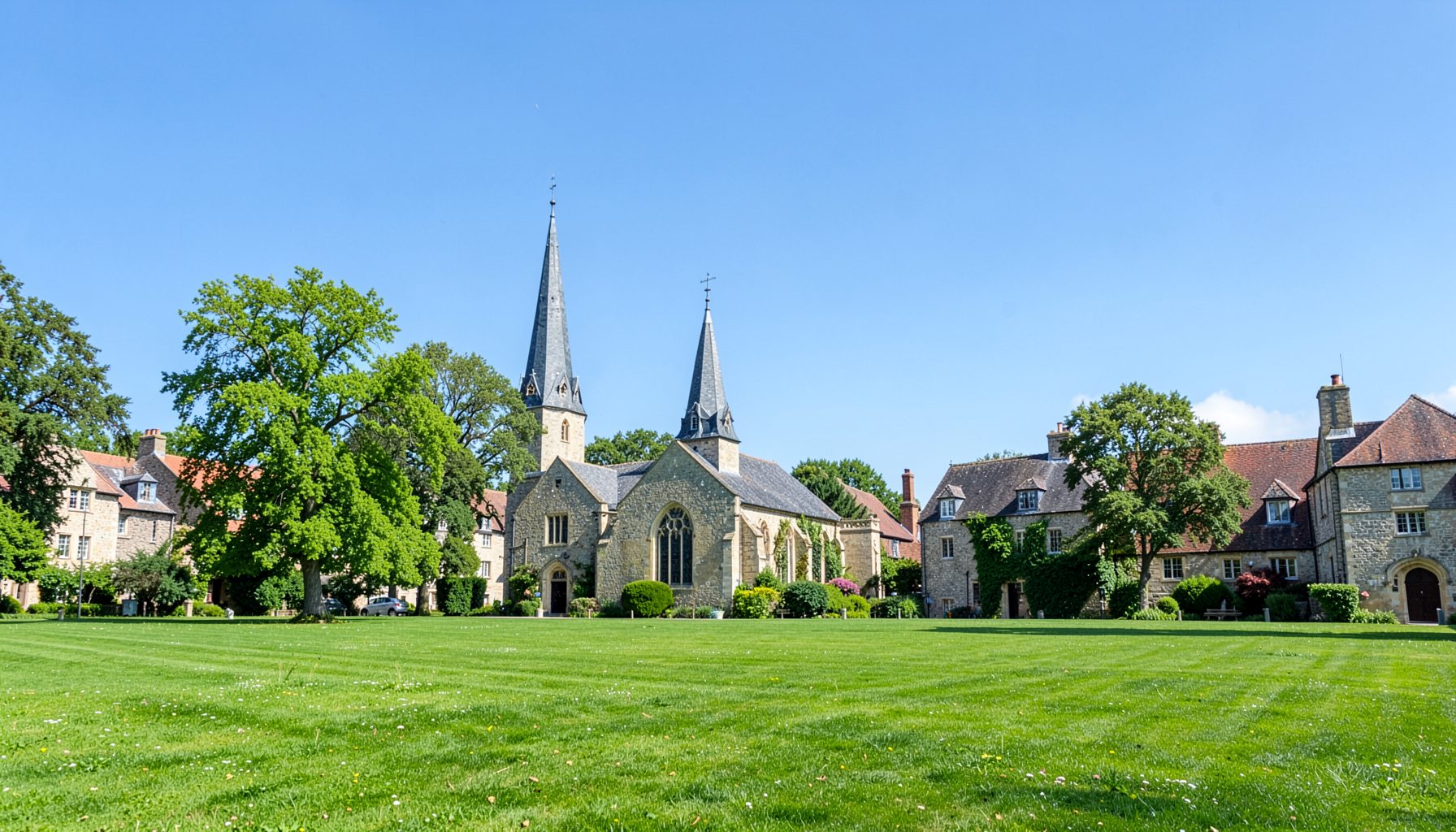A green parkland with a church spire and stone village buildings in the background under a clear blue sky